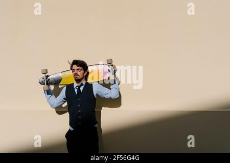 Businessman with eyes closed holding longboard behind head against wall Stock Photo