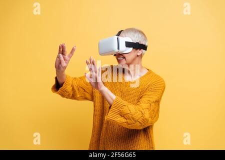 Woman gesturing while using virtual reality headset standing against yellow background Stock Photo