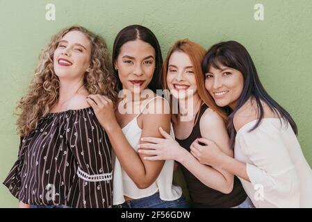 Happy multi ethnic friends standing against green wall Stock Photo