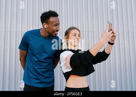 Female athlete with man taking selfie through mobile phone while standing against wall Stock Photo