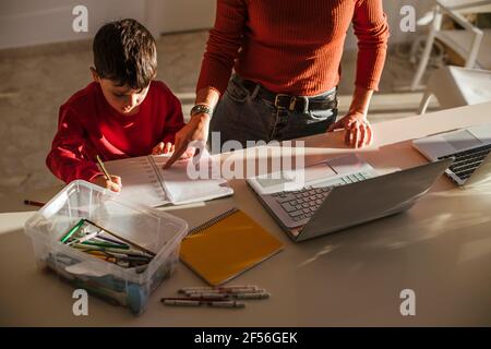 Mother assisting son in studies at dining table at home Stock Photo