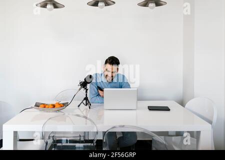 Businessman with microphone using laptop while sitting by table at home Stock Photo