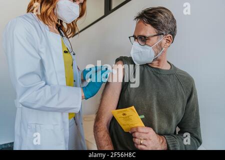 Female doctor putting adhesive bandage on patient arm while standing at examination room Stock Photo