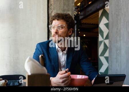 Thoughtful businessman with eyeglasses looking away while having food at cafe Stock Photo
