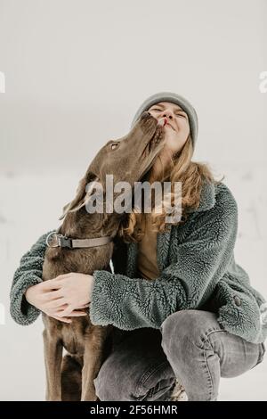 Portrait of teenage girl crouching in snow and embracing Labrador Retriever Stock Photo