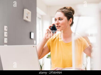 Female entrepreneur talking on smart phone while working at home Stock Photo