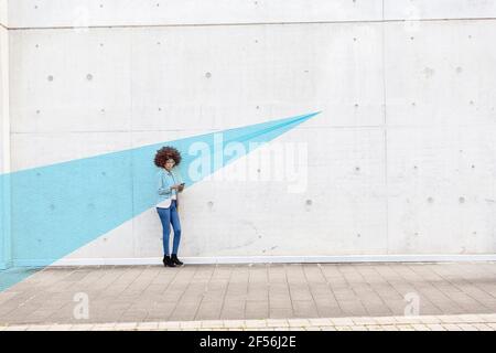 Young woman standing outdoors with smart phone in hands covered in blue facial recognition effect Stock Photo