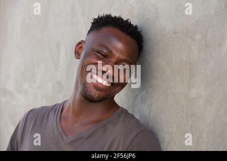 Close up portrait of happy young african man leaning against wall Stock Photo