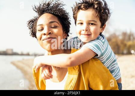Smiling mother piggybacking son on sunny day Stock Photo