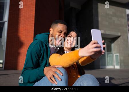 Young man making face while girlfriend taking selfie through smart phone Stock Photo