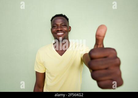 Wide angle portrait of african man gesturing thumbs up sign by green wall Stock Photo