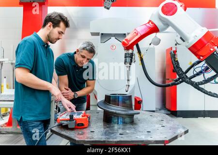 Young male engineer using control by colleague at robotics in factory Stock Photo