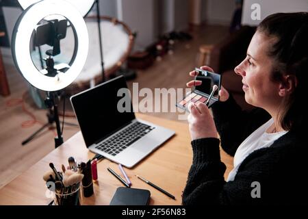 Smiling woman holding Make-up Palette while recording make-up tutorial at home Stock Photo