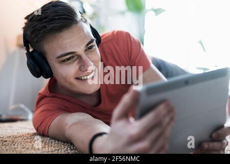 Smiling young man wearing wireless headphones while watching video on digital tablet Stock Photo