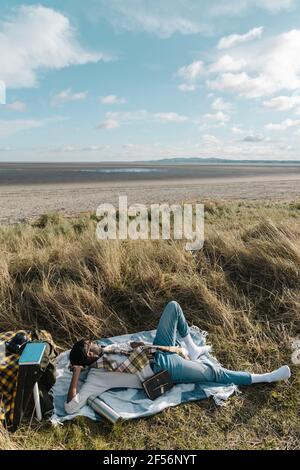 Young man lying on blanket while looking away at beach Stock Photo