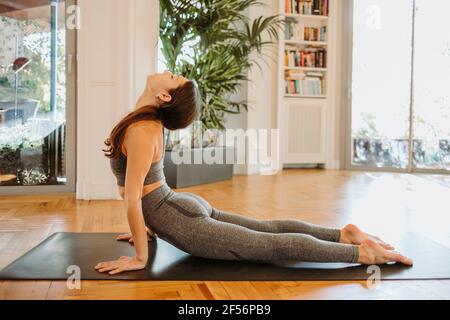 Active woman practicing upward facing dog position on mat at home Stock Photo