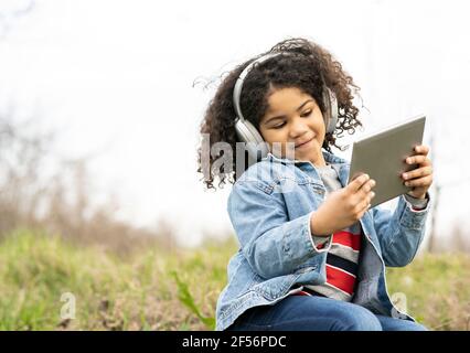 Cute boy listening music through headphones while using digital tablet in nature Stock Photo