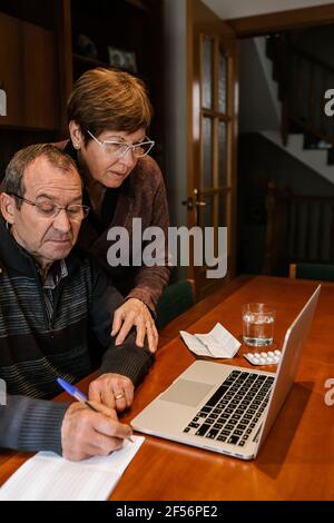 Senior man with social worker writing on book while using laptop at home during Stock Photo