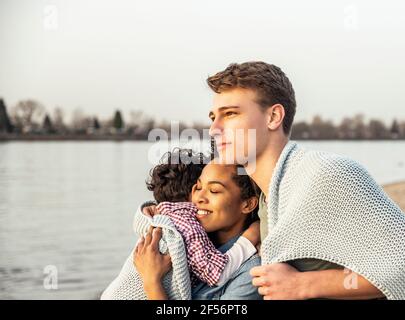 Young man covered in blanket standing by woman and boy by lake Stock Photo