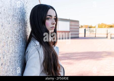 Thoughtful female teenager against wall on footpath Stock Photo