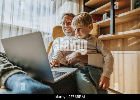 Boy using laptop while sitting with father on chair Stock Photo