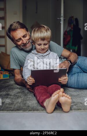 Smiling father watching son using tablet in bedroom Stock Photo