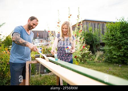 Happy couple painting wooden plank in garden Stock Photo