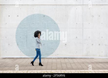 Visualization of data coming out of smart phone used by young woman walking along sidewalk Stock Photo