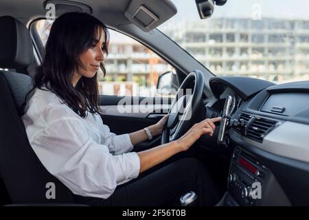 Young woman setting up global positioning system through smart phone while sitting in car Stock Photo