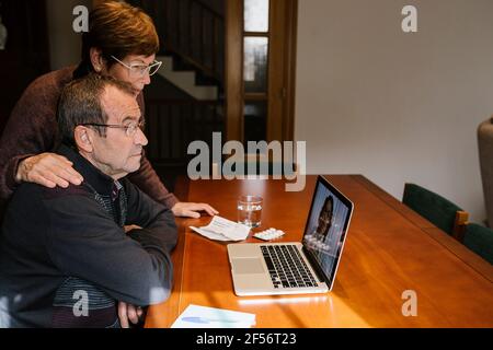 Female social worker standing by senior man consulting with female doctor through video call on laptop Stock Photo