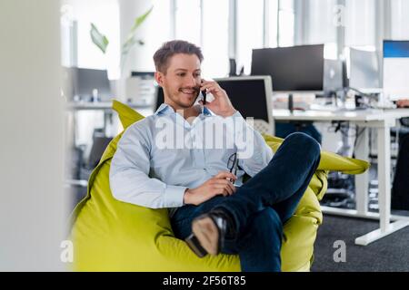 Male entrepreneur talking through mobile phone while sitting on bean bag at office Stock Photo