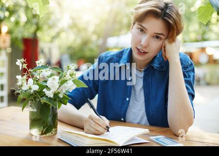 Woman writing in diary. Portrait of a girl taking notes in her notepad outdoors planning a trip or vacation or future business looking at camera Stock Photo