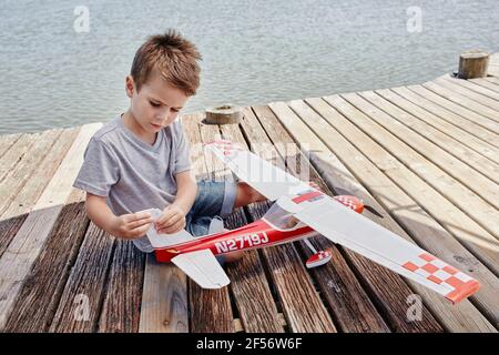 Boy checking airplane toy while sitting on pier Stock Photo