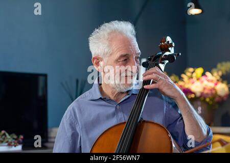 Smiling senior man playing cello at home Stock Photo