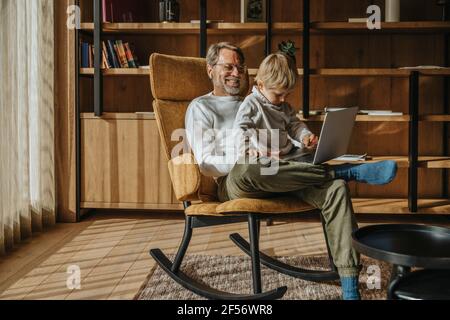 Boy using laptop while sitting with father on chair Stock Photo