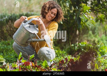 Happy woman watering plants in permaculture garden Stock Photo