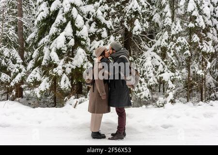 Young couple with backpack kissing while standing in forest Stock Photo