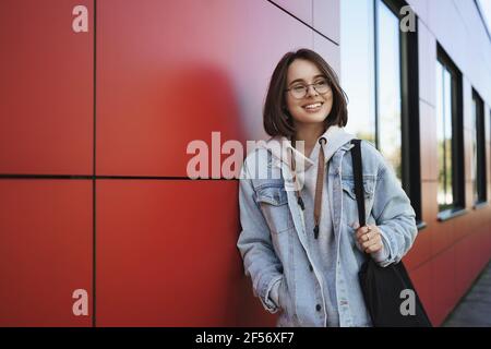 Young generation, lifestyle and education concept. Outdoor portrait of happy girl on her way home after classes, looking sideways dreamy and happy Stock Photo