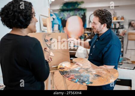 Mature artist teaching painting to young female painter at art studio Stock Photo