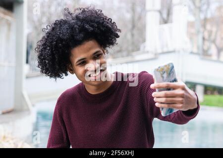 Smiling boy taking selfie on mobile phone while sitting outdoors Stock Photo