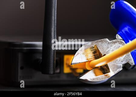 Tearing and cutting with blue wire cutters the network connection of the yellow wire of the Internet connection. Disabling and restricting Internet ac Stock Photo