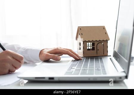 The real estate agent works at the laptop. A model house on a realtor's desk. Stock Photo