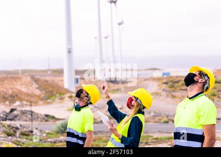 Woman engineer and skilled workers holding yellow safety helmet with standing and checking wind turbine power in construction site renewable energy. C Stock Photo
