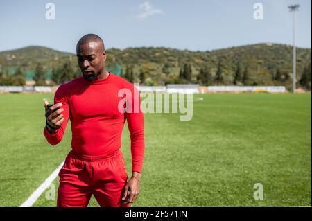 Front view of black sportsman in a football field walking while checking times with a stopwatch. Serious concentrated face. Stock Photo