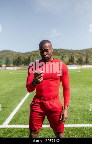 Front view of black sportsman in a football field training and holding a timer checking times. Stock Photo