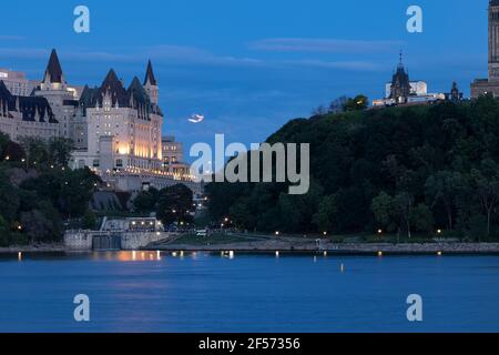 Historic Chateau Laurier and downtown Ottawa at night from across the river. Blue night sky with a full moon partially covered by a cloud at twilight. Stock Photo