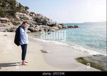 Latin businessman with suit take off jacket with barefoot standing on the shore in beautiful beach. Desire for freedom concept. Stock Photo