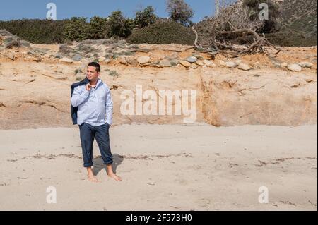 Latin businessman in suit take off jacket and enjoy the peace on the beach. Burnout, escape from city life stress. Stock Photo