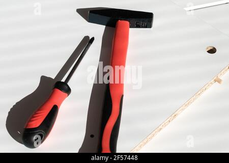 A hammer and a screwdriver on a white wooden surface. Red handles tools Stock Photo