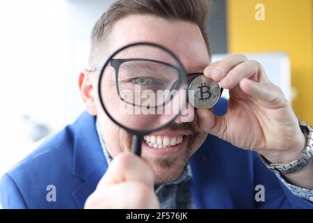 Man looks through magnifying glass and holds bitcoin in his hand Stock Photo